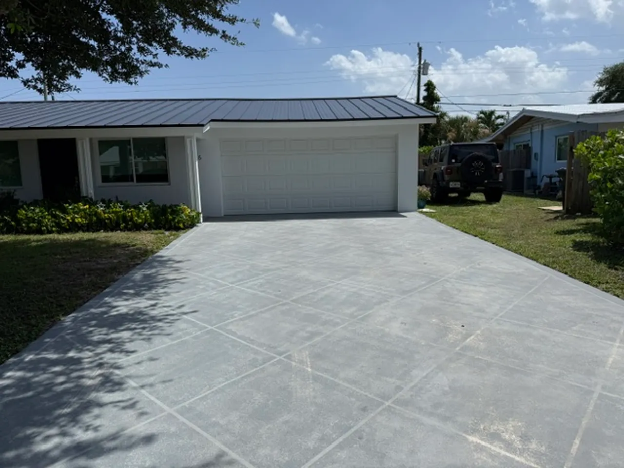 Freshly cleaned concrete driveway in front of a white home with a black metal roof