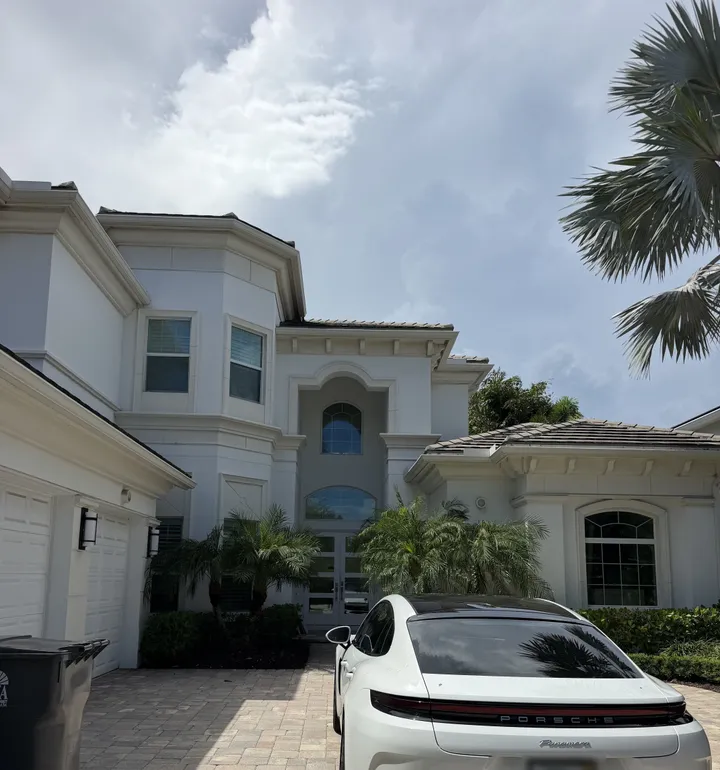 Clean white two-story stucco home with a paver driveway and palms