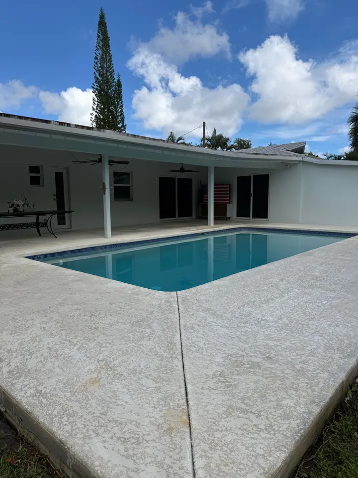 Bright, clean concrete pool deck and covered patio behind a white home