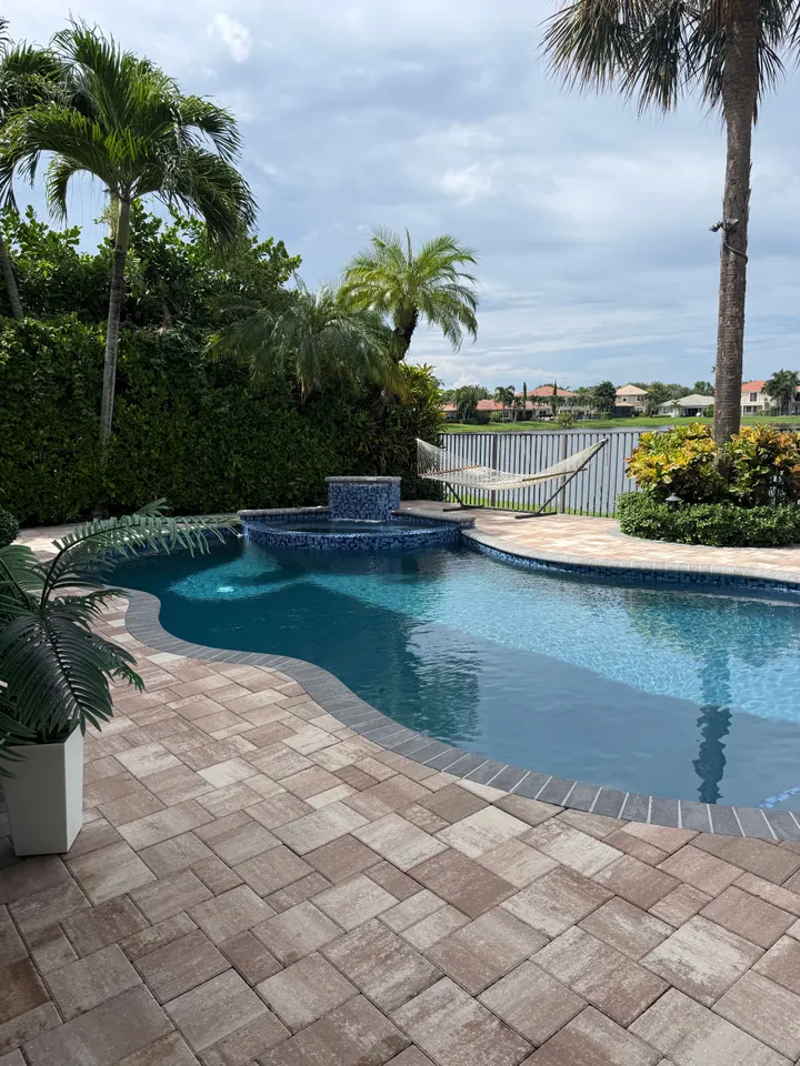 Clean paver pool patio beside a freeform pool with a spa and lake view
