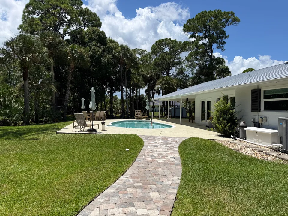 Clean paver walkway leading to a bright pool deck behind a white home