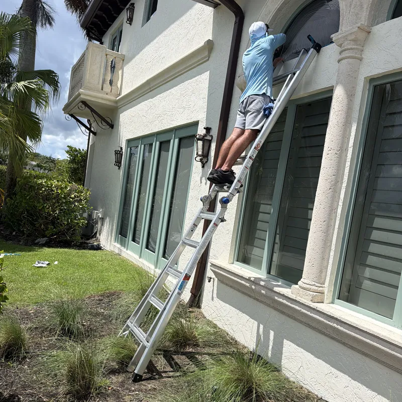 Cooper on a ladder cleaning a tall arched window on a Mediterranean-style home